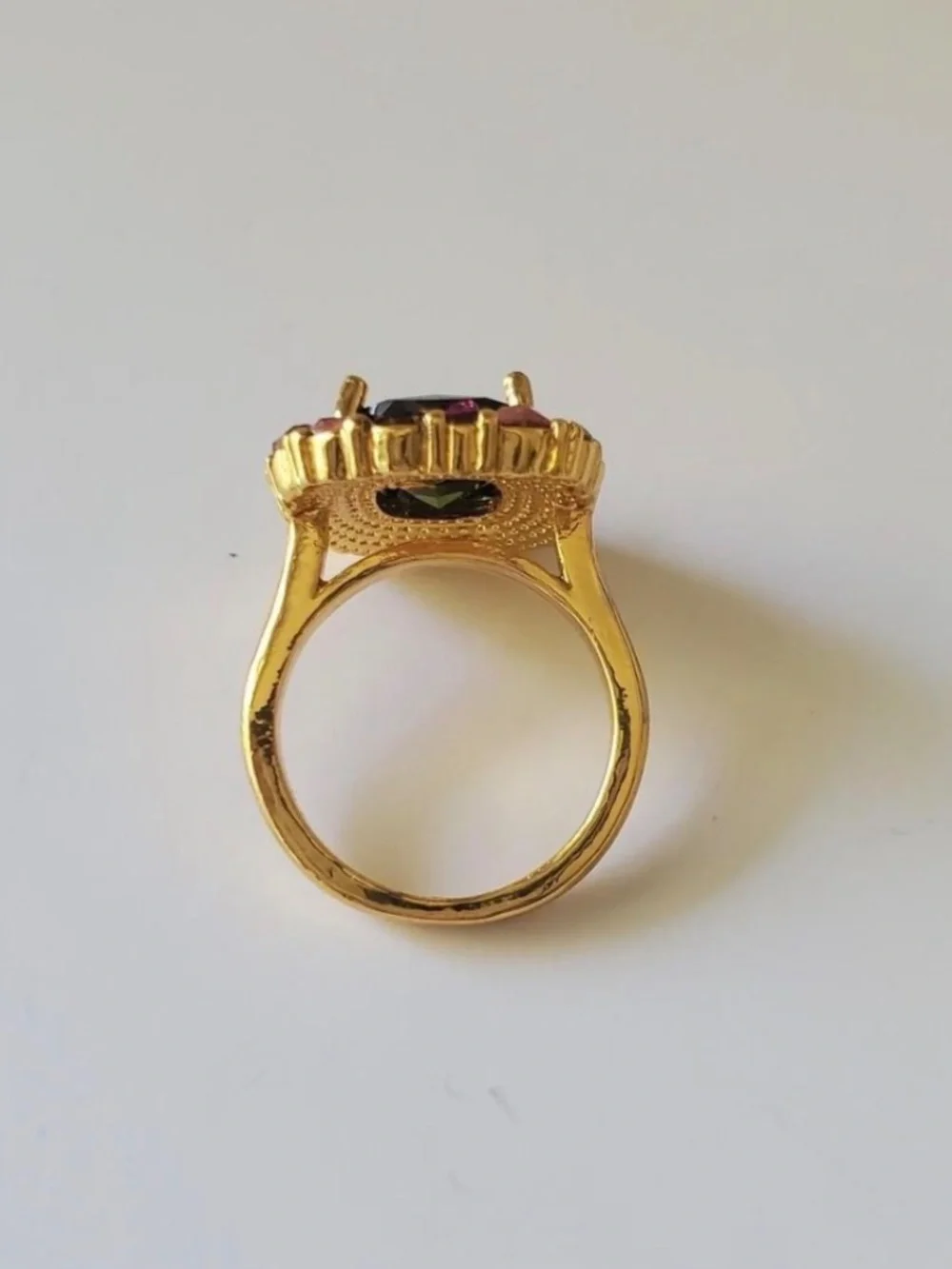Gold ring with green central gemstone surrounded by pink and red rhinestones